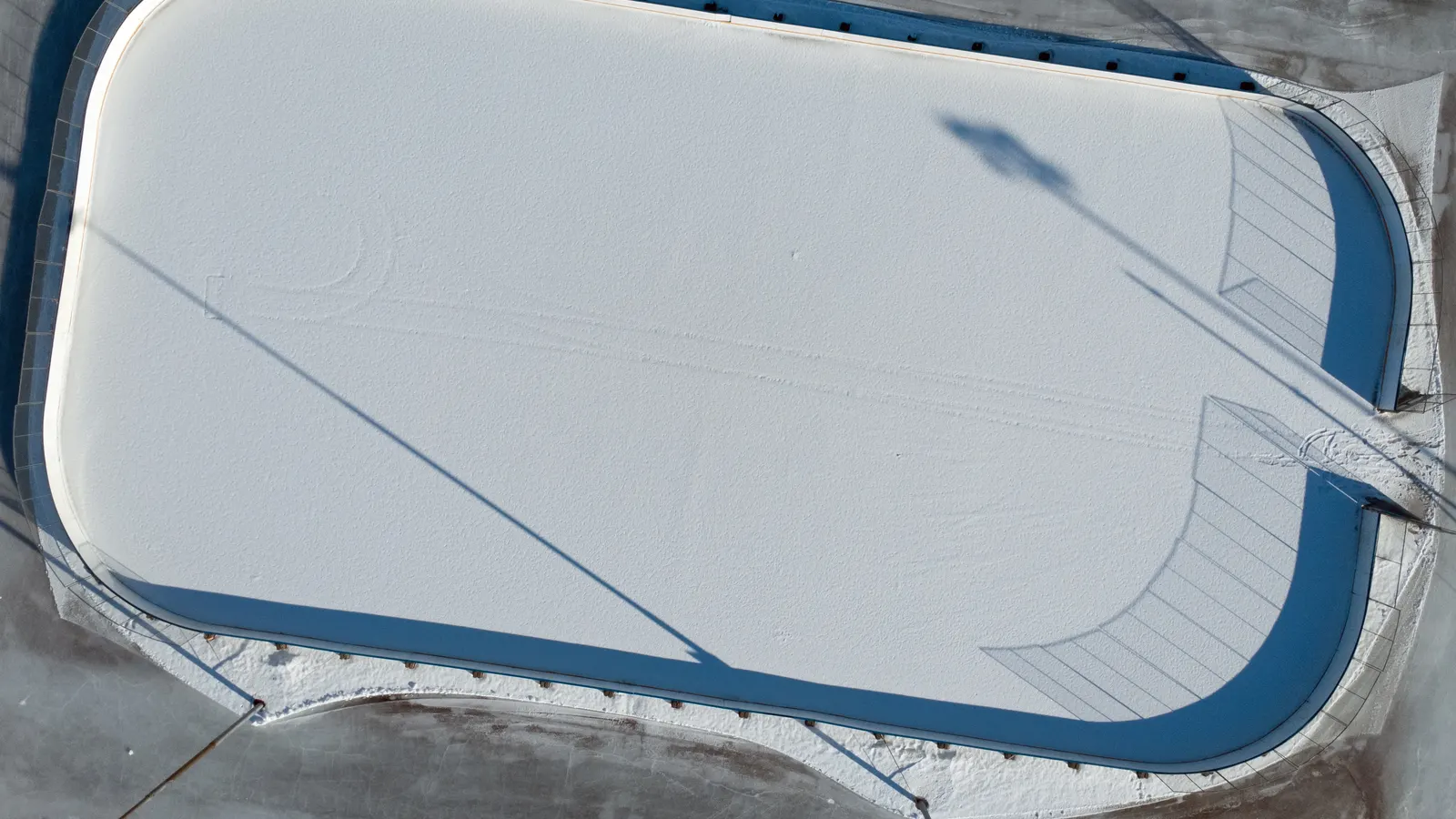 Patinoire de hockey enneigée vue du ciel, avec bandes bleues et filets visibles